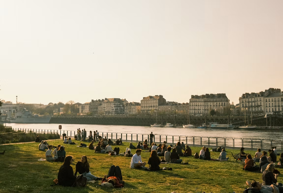 Les bords de Loire à Nantes au coucher du soleil, des groupes de personnes assises sur la pelouse.