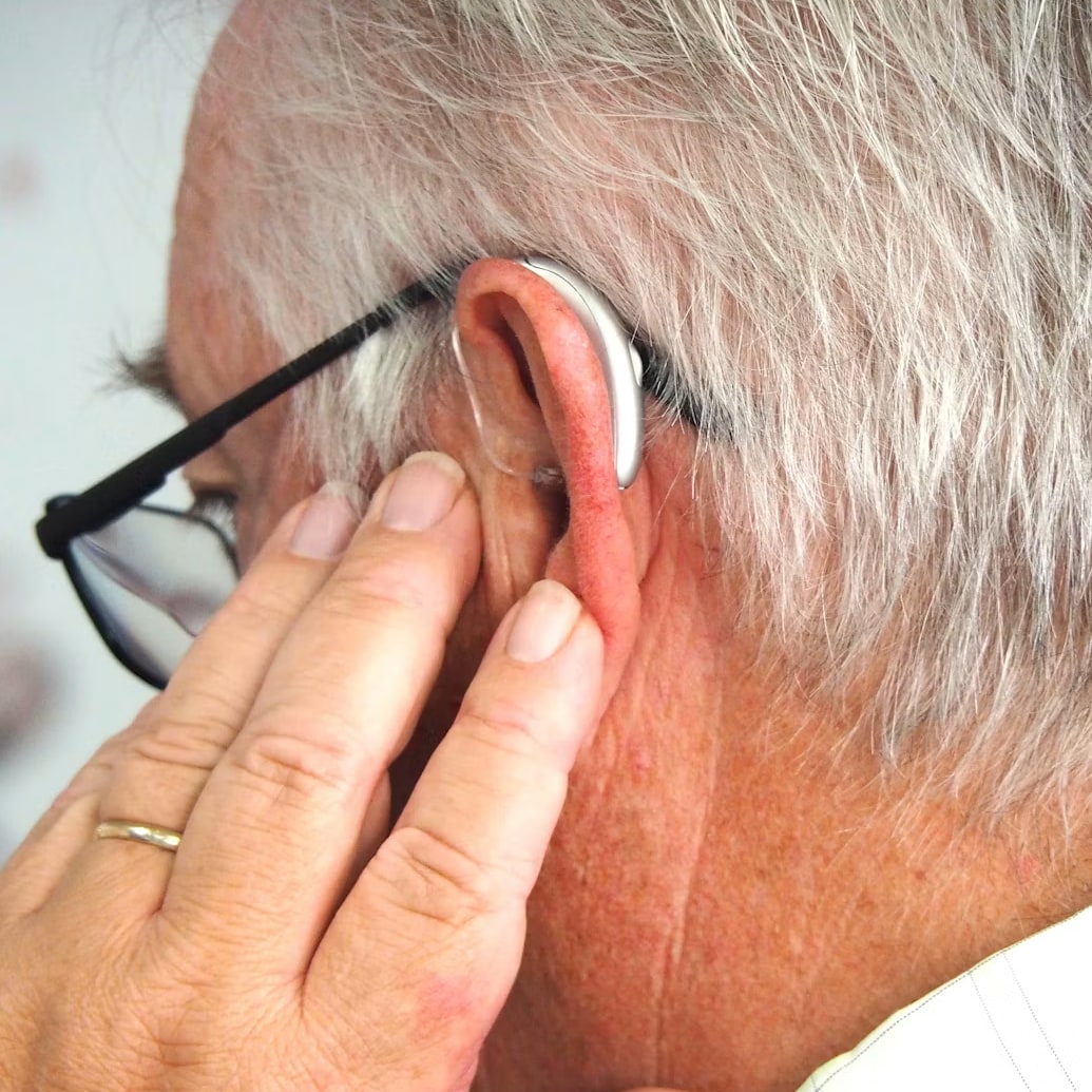 Gros plan sur l'oreille d'un homme réglant son aide auditive