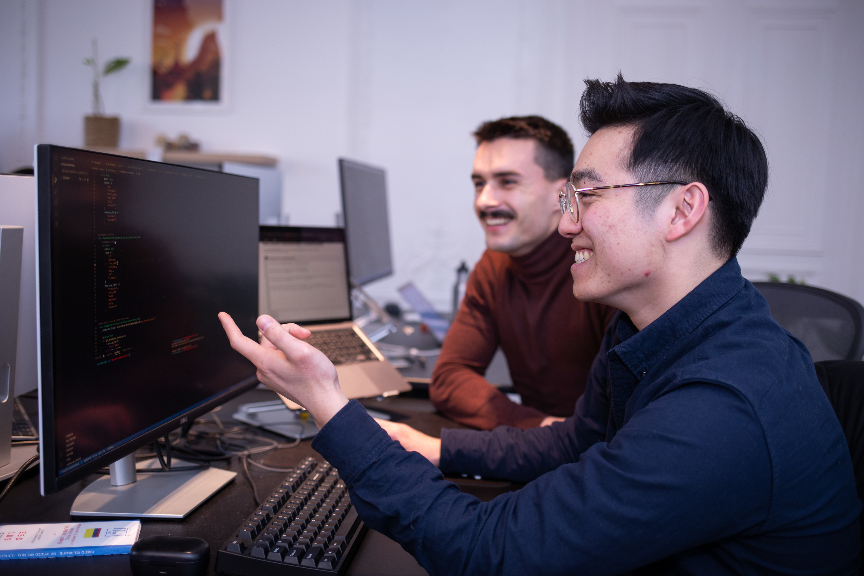 Deux développeurs souriants travaillent ensemble devant un écran affichant du code
