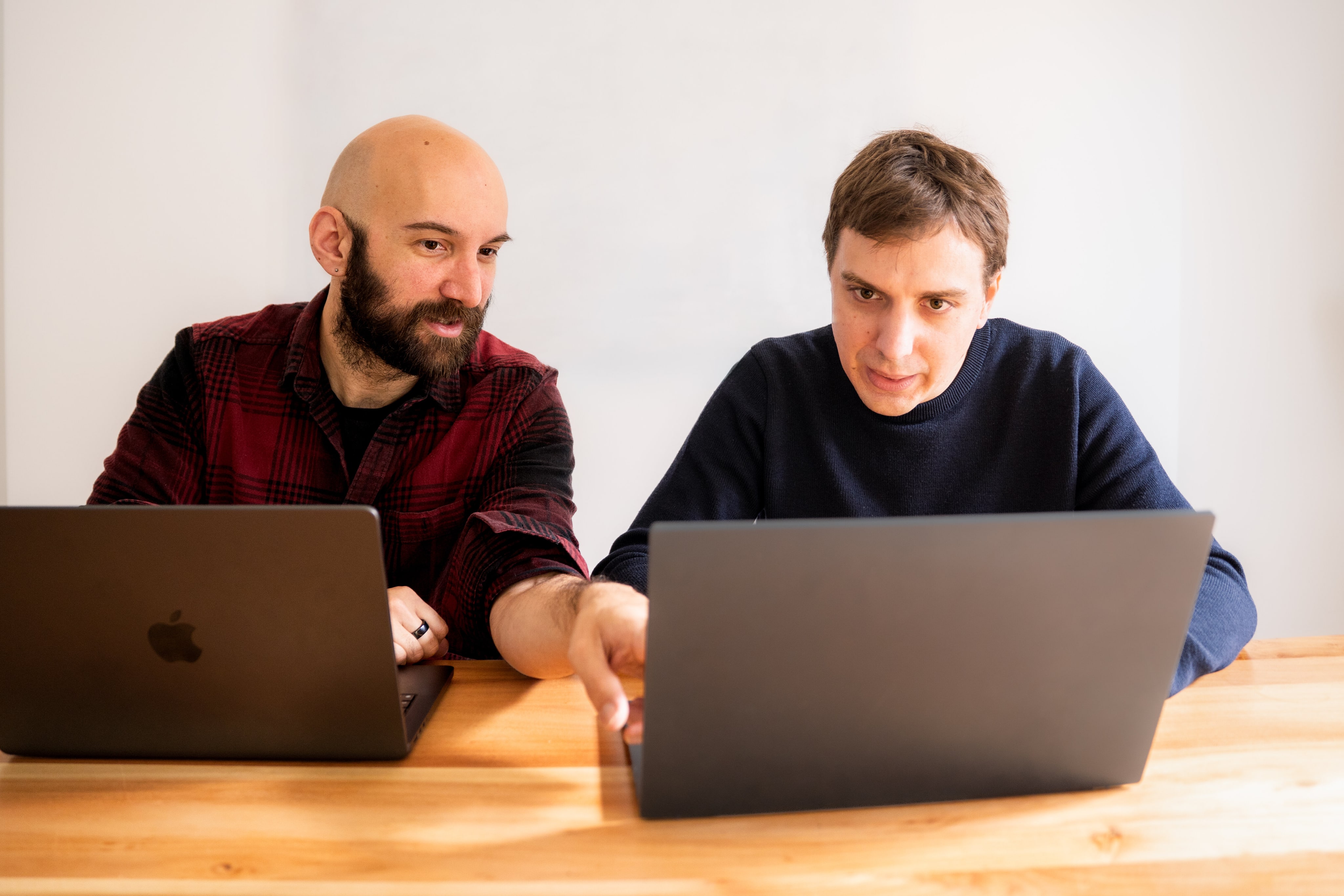 Deux développeurs côte à côte devant leurs ordinateurs portables, l'un montrant quelque chose à l'écran de l'autre.